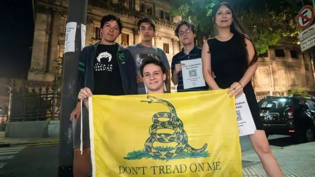 Jovens posando para foto à noite; um deles segurando uma Bandeira de Gadsden