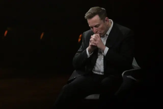 Elon Musk com a mão na boca e cabeça baixa