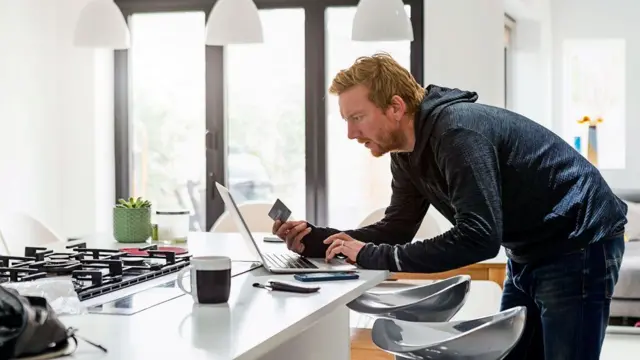 Homem com cartão de crédito na mão olhando para laptop