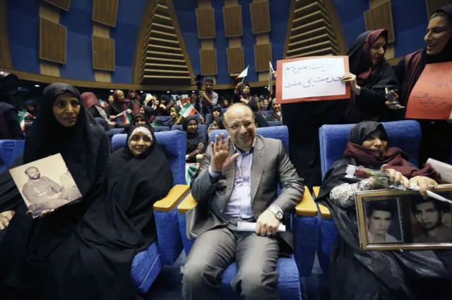 Mohammad Bagher Ghalibaf sentado em auditório, rodeado por mulheres; ele acena e sorri 