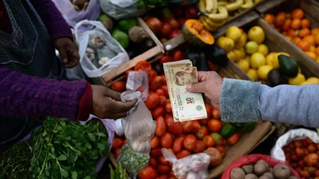 Uma pessoa pagando com pesos argentinos em um mercado de frutas e vegetais