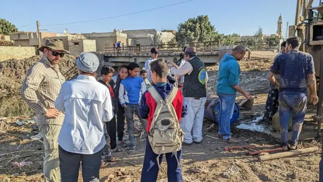 Pesquisadores entre crianças em um sítio arqueológico no Egito