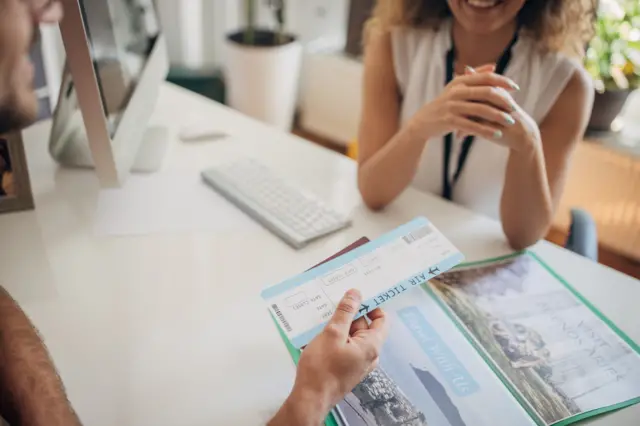 Homem entrega passagem para mulher em agência de turismo genérica