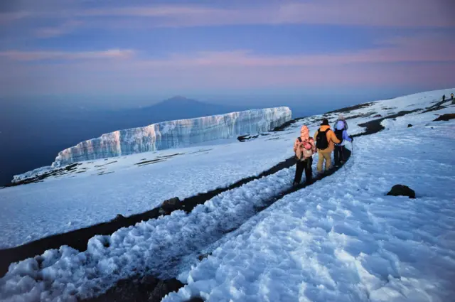 Grupo de pessoas caminhando entre geleiras de alta altitude em direção ao cume do Monte Kilimanjaro, no Parque Nacional Kilimanjaro, na Tanzânia nzania - stock photo