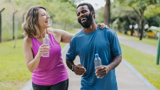 Mulher e homem sorriem durante caminhada em parque