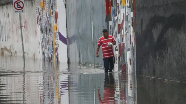 Homem andando em rua lagada após temporal em São Paulo