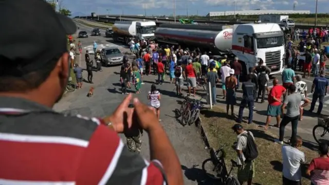 Em foto de 2018, homem observa dezenas de manifestantes em volta de caminhão parado em estrada do Rio