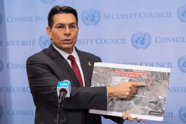 O Embaixador Danny Danon, O embaixador de Israel na ONU, fala durante uma declaração à imprensa antes da reunião do Conselho de Segurança. Ele segura imagens de satélite de lançadores de foguetes pertencentes ao Hezbollah, localizados a cerca de 150 metros das forças da ONU.