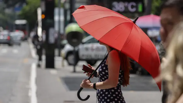 Mulher andando com guarda-chuva para se proteger do sol forte