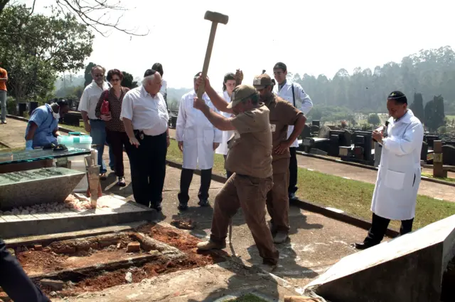 Funcionário do cemitério usando marreta para golpear túmulo