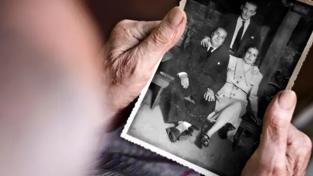 Mãos de pessoa idosa segurando foto antiga de família em preto e branco