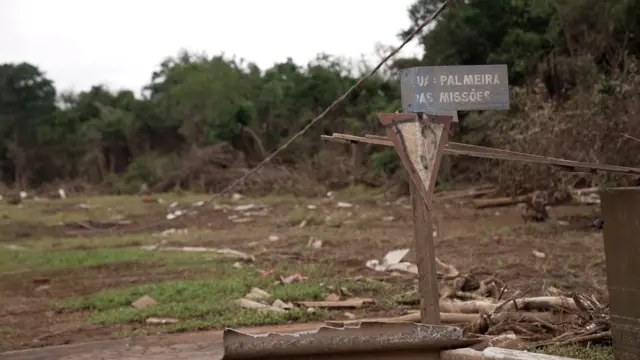 Placa deteriorada com nome de rua e escombros em volta de terreno