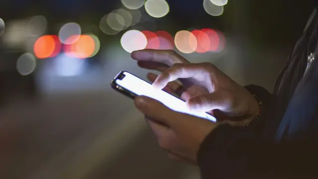 Mão de alguém usando celular na rua à noite