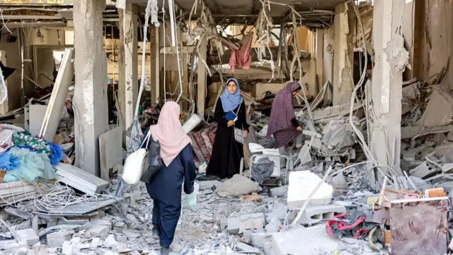 Mulheres andam nos escombros de uma loja de roupas destruída em um prédio residencial atingido por bombardeios israelenses, no bairro de Daraj, na cidade de Gaza, em 14 de junho de 2024, em meio ao conflito em curso entre Israel e o Hamas