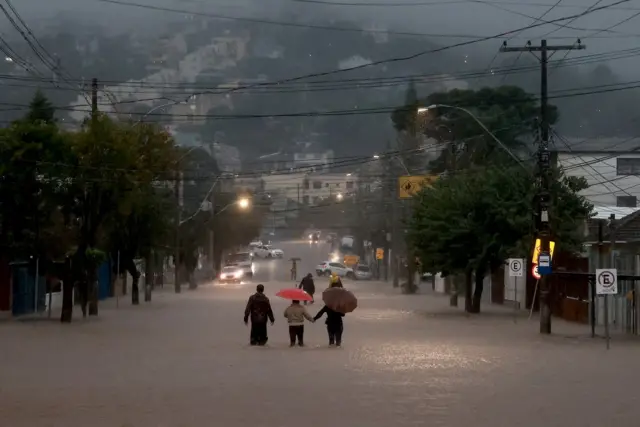 Pedestres caminham em rua alagada