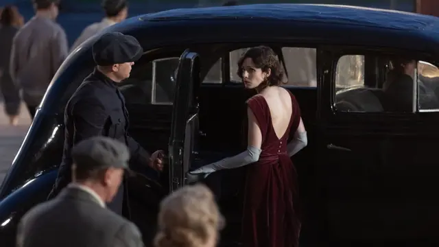 Mulher entrando em carro, enquanto homem abre a porta do veículo para ela 
