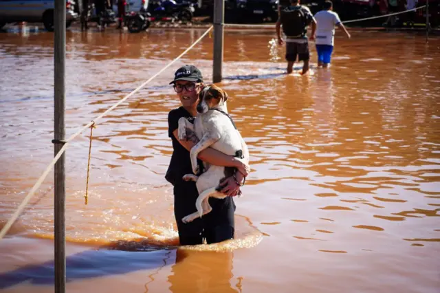 Mulher segurando cachorro no colo em meio à enchente