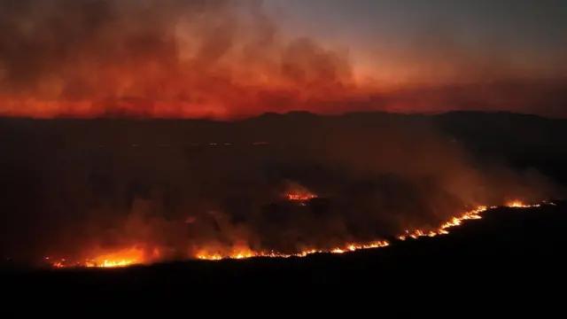 Imagem feita de drone mostra uma grande área pegando fogo durante a noite.