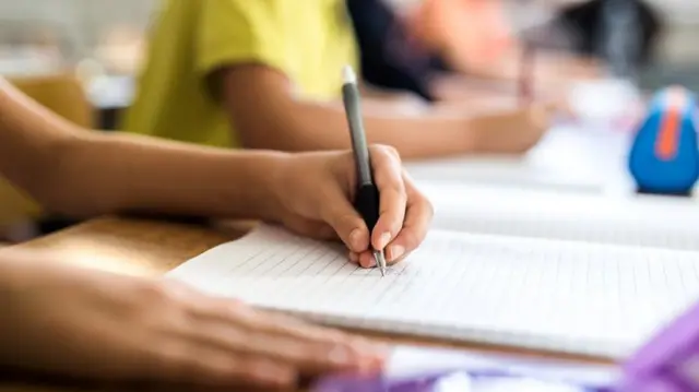 Mão de criança escrevendo no caderno em sala de aula