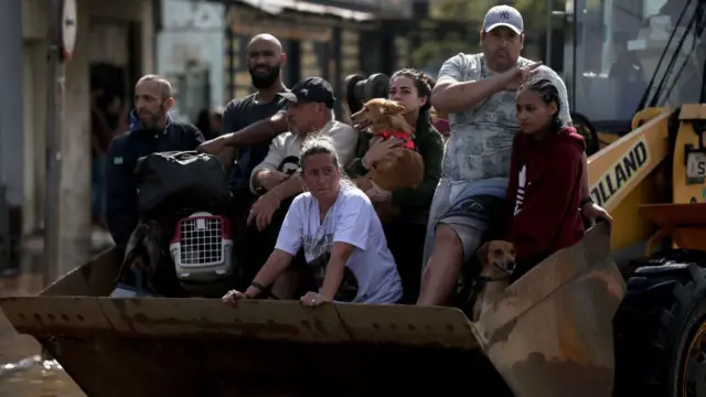 Pessoas em cima de trator sendo transportadas de área alagada