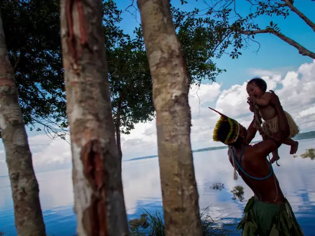  Um homem indígena Dessana brinca com um bebê próximo ao Rio Negro na Reserva Tupe nos arredores de Manaus, Amazonas