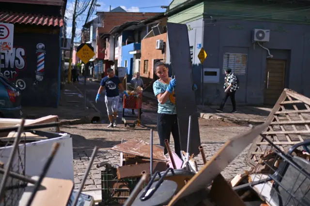 Moradores trabalham na limpeza de uma rua em uma área onde o nível das águas baixou no bairro Menino Deus, em Porto Alegre, em 17 de maio de 2024