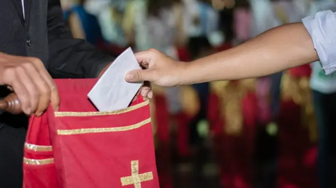 Pessoa colocando doação no saco de oferendas para a igreja