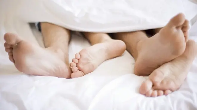 Unidentified young couple in bed, sleeping, sleep, embrace beneath a duvet, bare feet sticking out