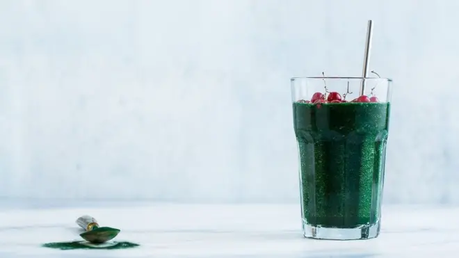 Soothie de suco verde com spirulina ao lado de colher de spirulina