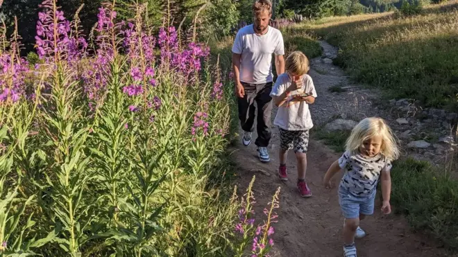 Um homem branco caminha com seus dois filhos ao lado de um campo de lavandas