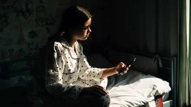 Uma jovem usa o telefone sentada na cama