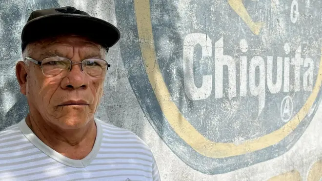 Isabel Coba Mojica next to a Chiquita sign on the wall of the old plantation where he worked in Panama