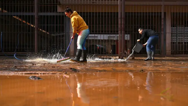 Duas pessoas fazem limpeza de calçada 
