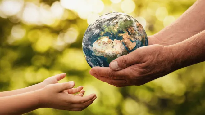 Un adulto pasando una esfera que representa la Tierra a las anos de un niño o niña