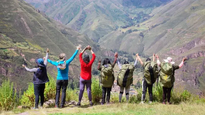 Carregadoras, guias e andarilhas de braços dados e observando a vista da Trilha Inca