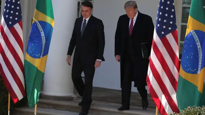 Jair Bolsonaro e Donald Trump descem escada rodeados por bandeiras dos EUA e do Brasil