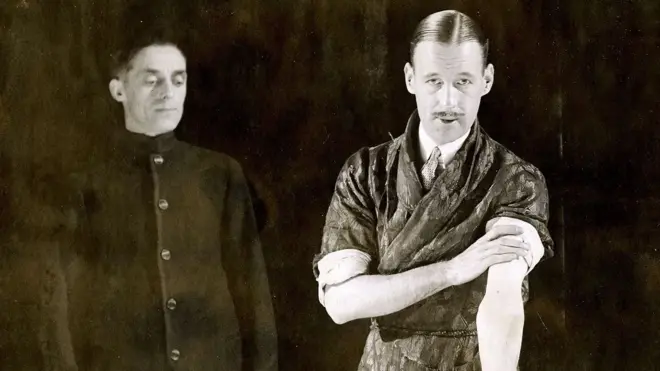 Foto em preto em branco dois homens brancos, um tem bigode pontudo e casaco estampado
