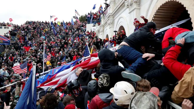 Multidão com bandeiras dos EUA em frente a estrutura externa do Capitólio