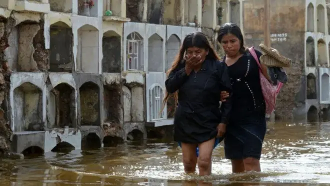 Duas mulheres caminham no Peru por uma área alagada pelas chuvas