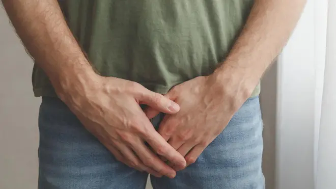 homem vestido com as mãos em frente ao pênis 