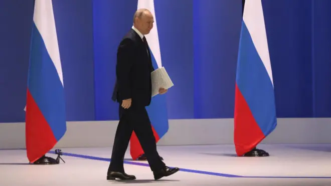 Vladimir Putin caminhando com bandeiras russas ao fundo
