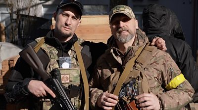 Men with guns, one wearing military fatigues, one black