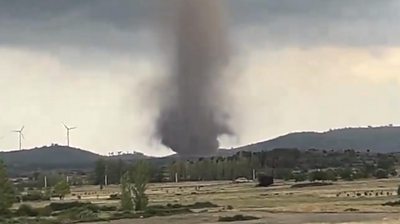 A large tornado on the horizon between hills and wind turbines