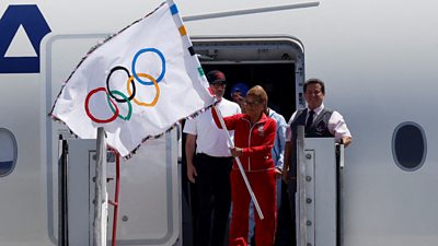 Mayor Karen Bass is holding the Olympic flag with a group of men behind her.