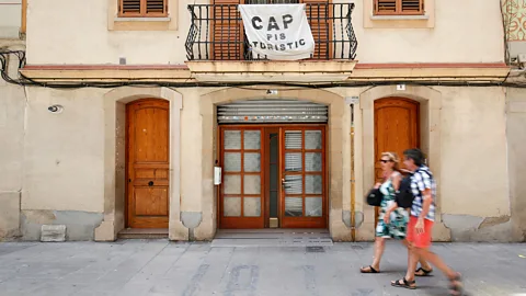 A couple walking under a banner reading "No tourist flats" in Barcelona (Credit: Getty Images)