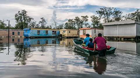 People on a small boat wading through flood waters in a neighbourhood (Credit: Getty Images)