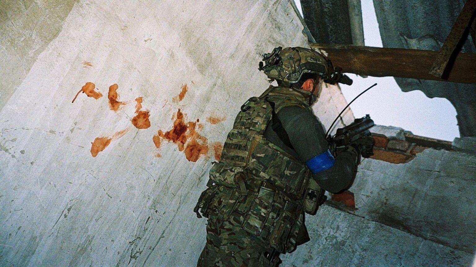 A soldier aims a gun next to a blood-splattered wall