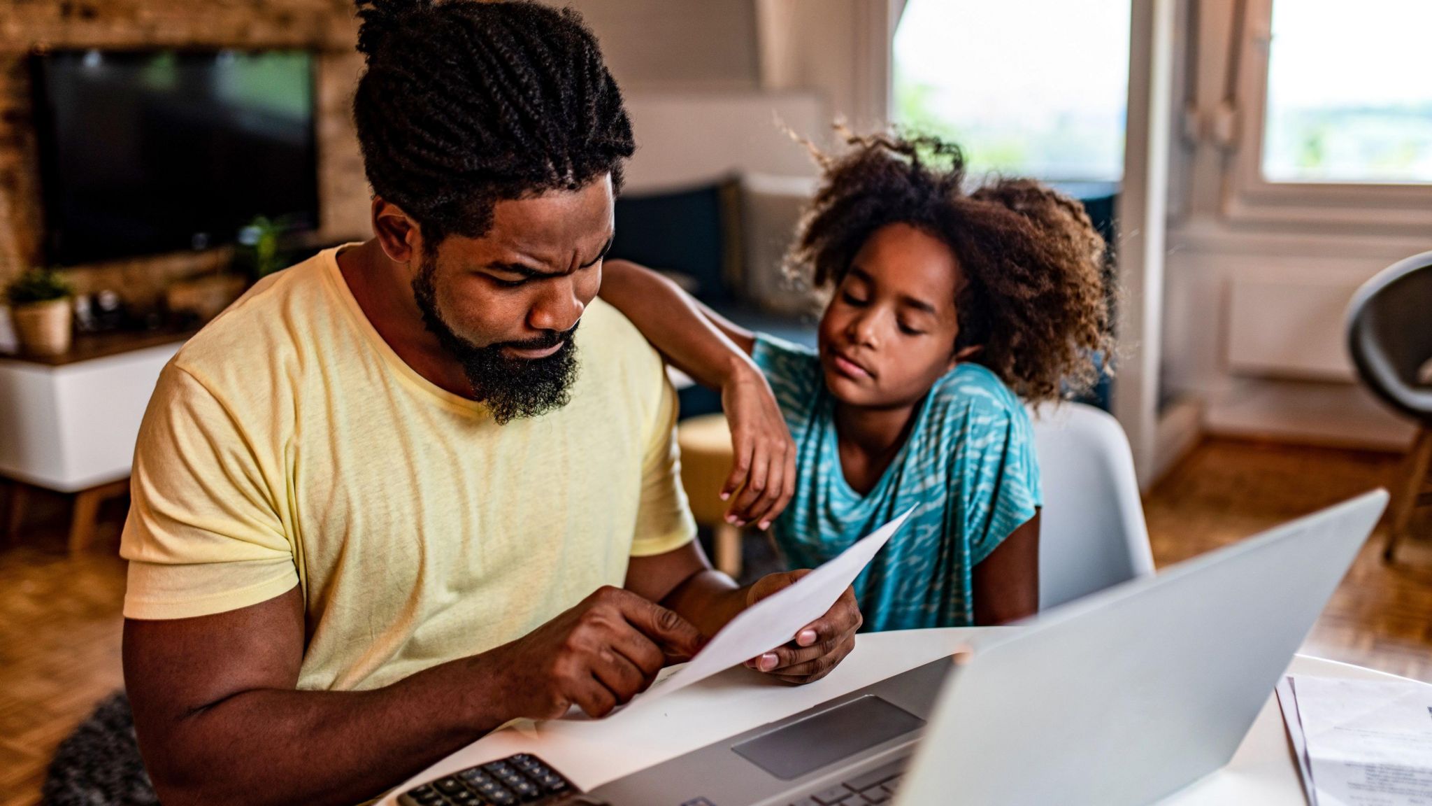 A father and his young daughter look worried whilst looking at bills