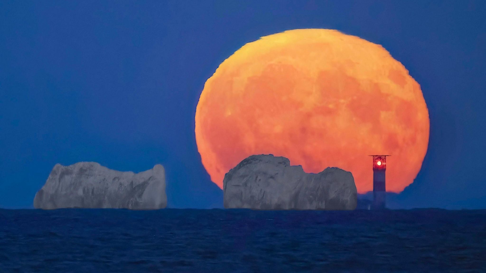 Large orange moon behind The Needles cliffs and lighthouse