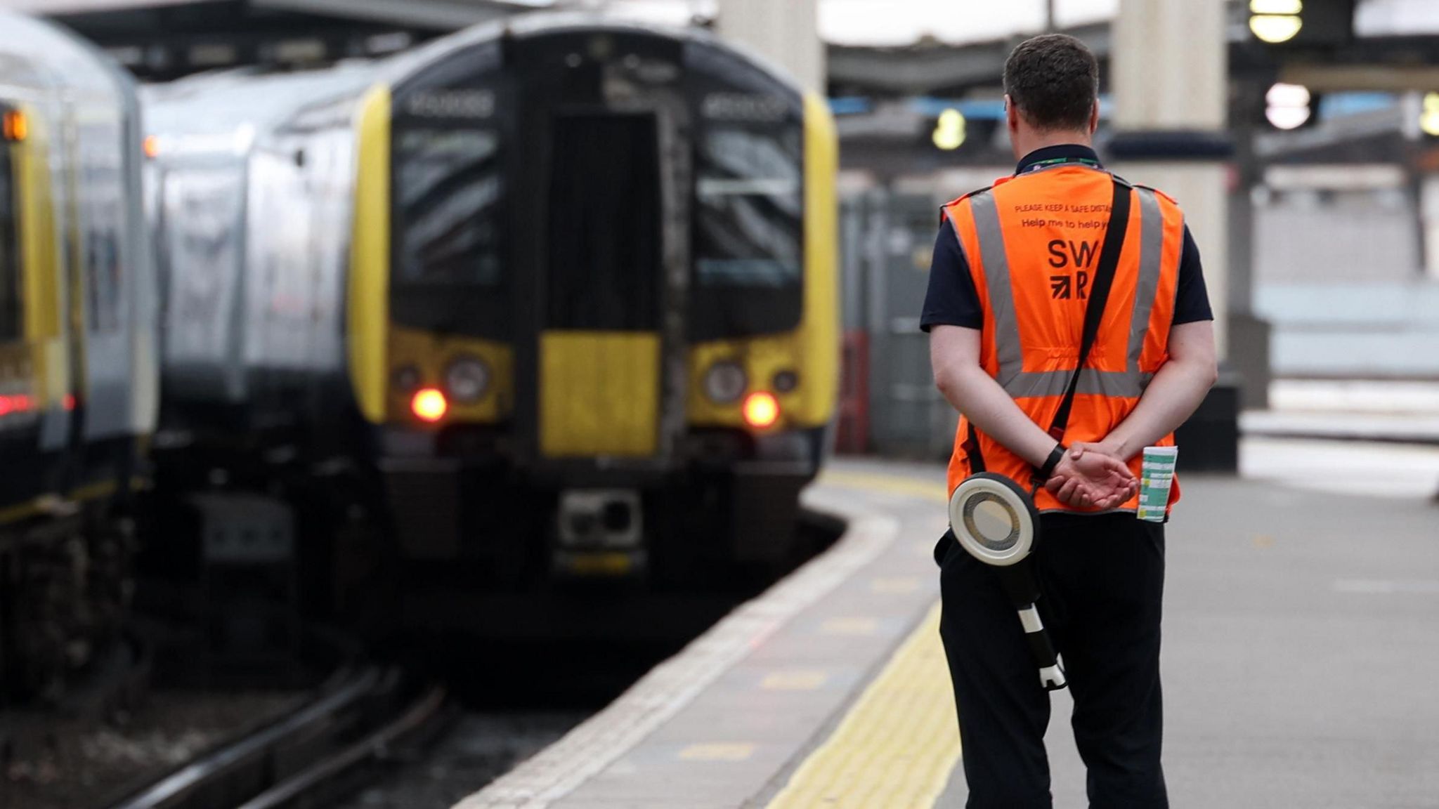 A waterloo station worker watches as a train approaches a platform